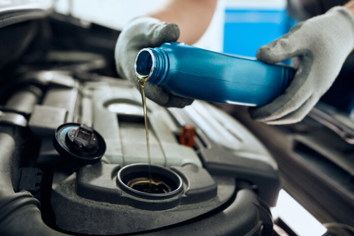 Nahaufnahme des Mechanikers, der Motoröl während der Autowartung in der Autowerkstatt gießt.